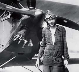 Amelia Earhart standing in front of a propellor plane