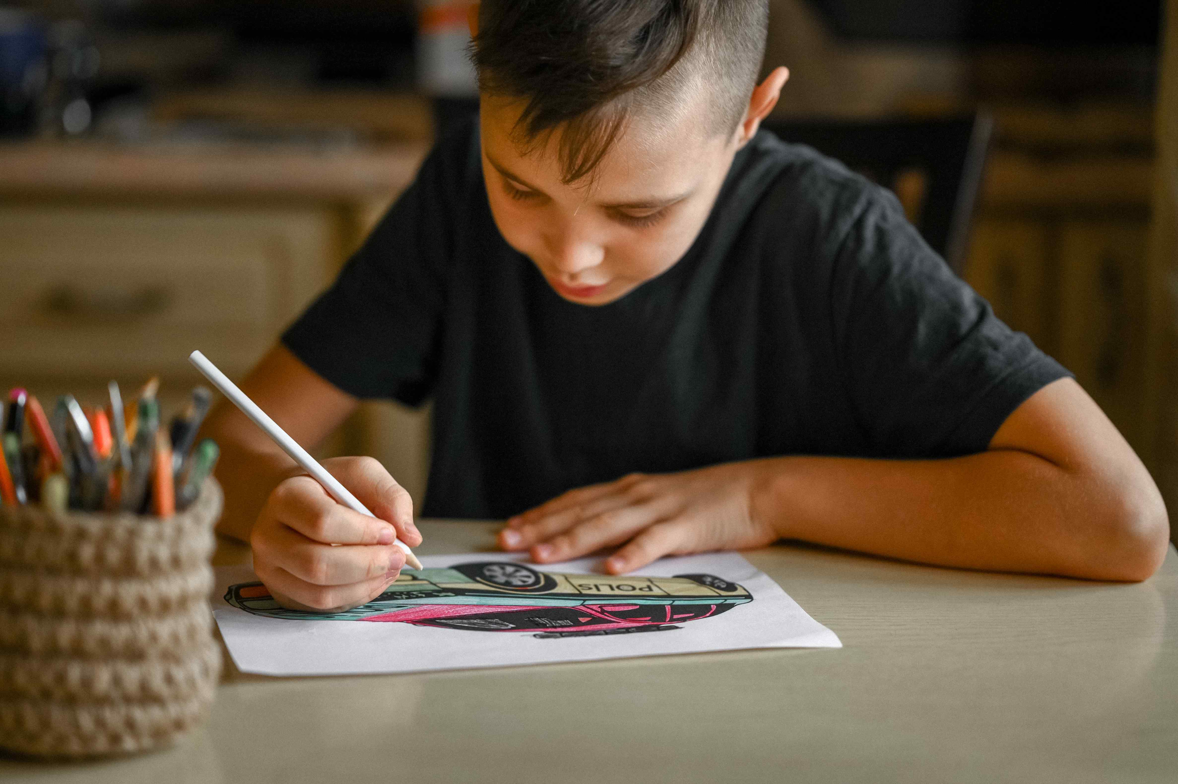 10-year-old boy sitting at a table, studiously using coloured pencils to draw a vibrant police car.