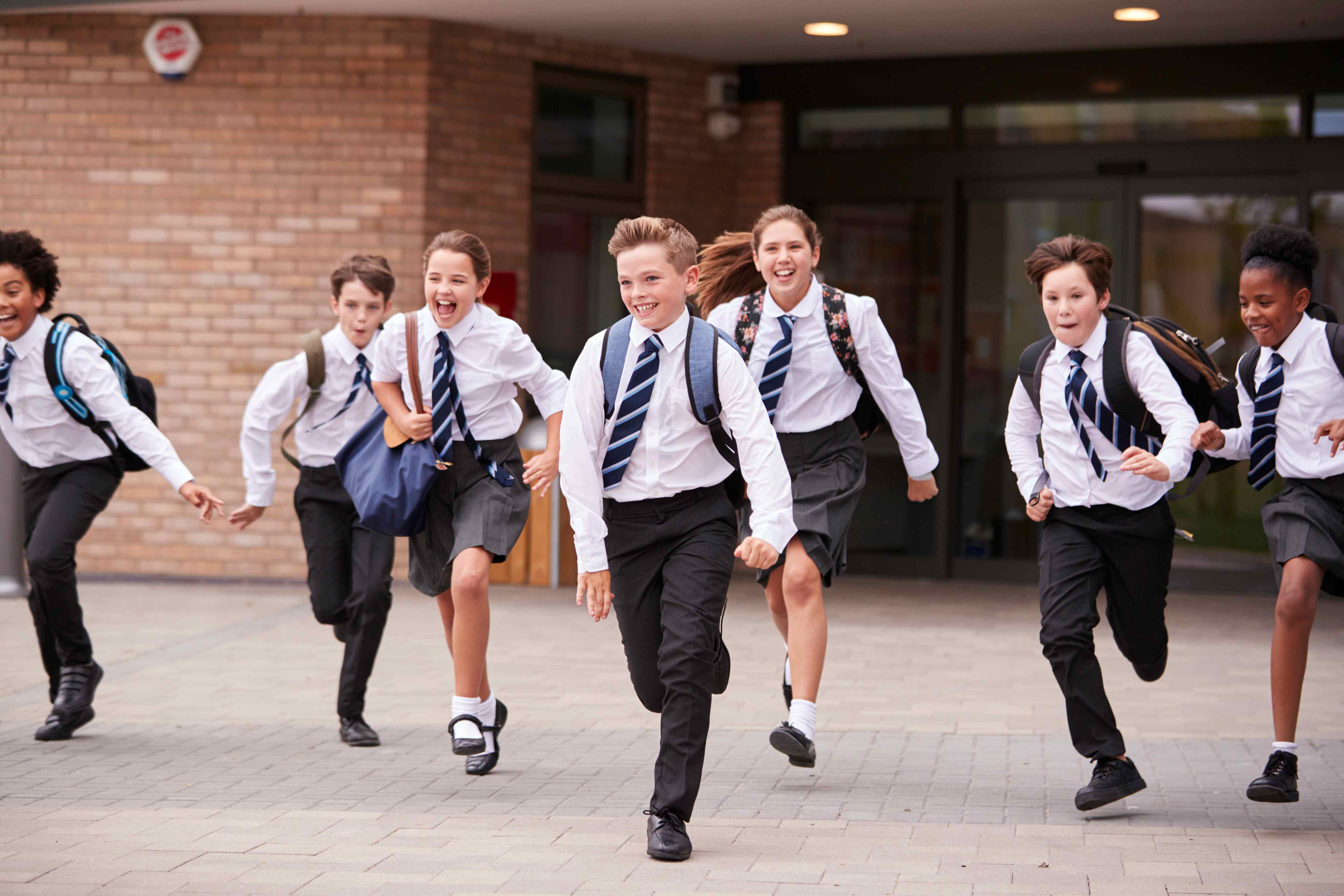 Children wearing British school uniform smiling and running out of a school building