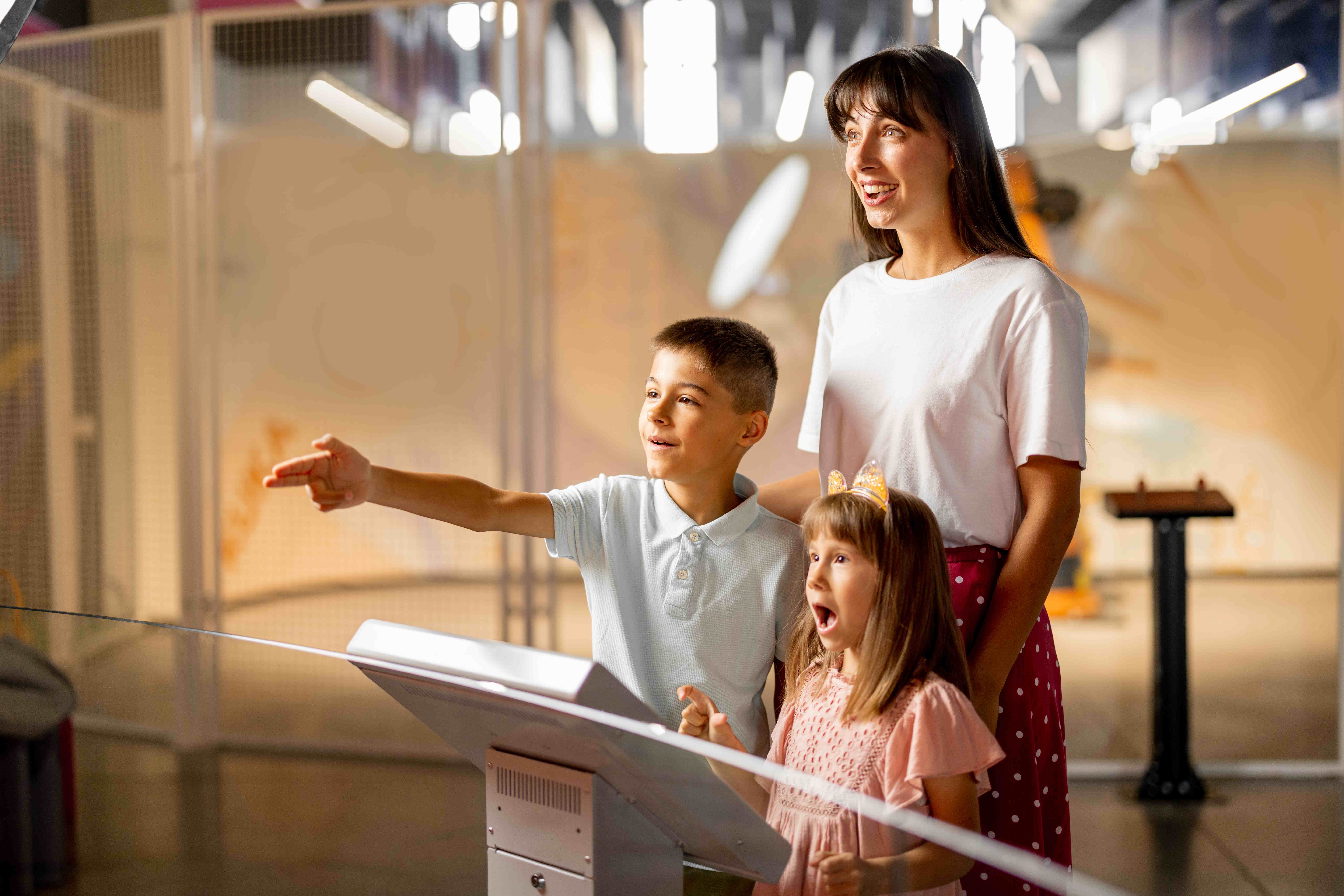 Mother with a young boy and girl standing in a museum exhibition, all looking in awe at something off-camera